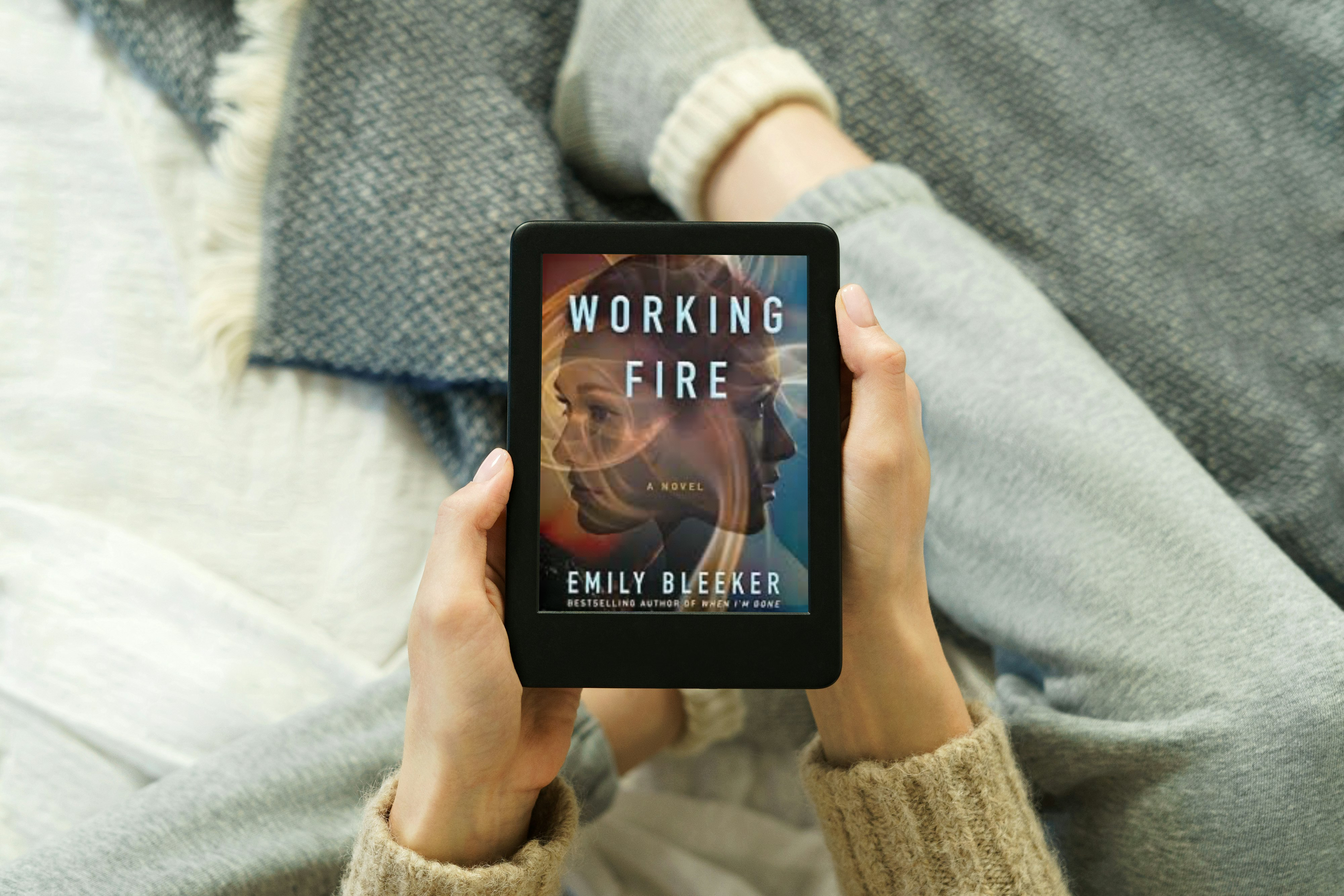 a photo of a woman holding an e-reader with the cover photo of working fire by emily bleeker displayed on the front