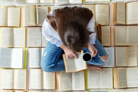 photo of woman reading a book while sitting on multiple books learning how to read on a budget