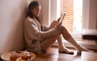 photo of woman sitting on the floor with a tray of tea beside her enjoying a spooky reading session