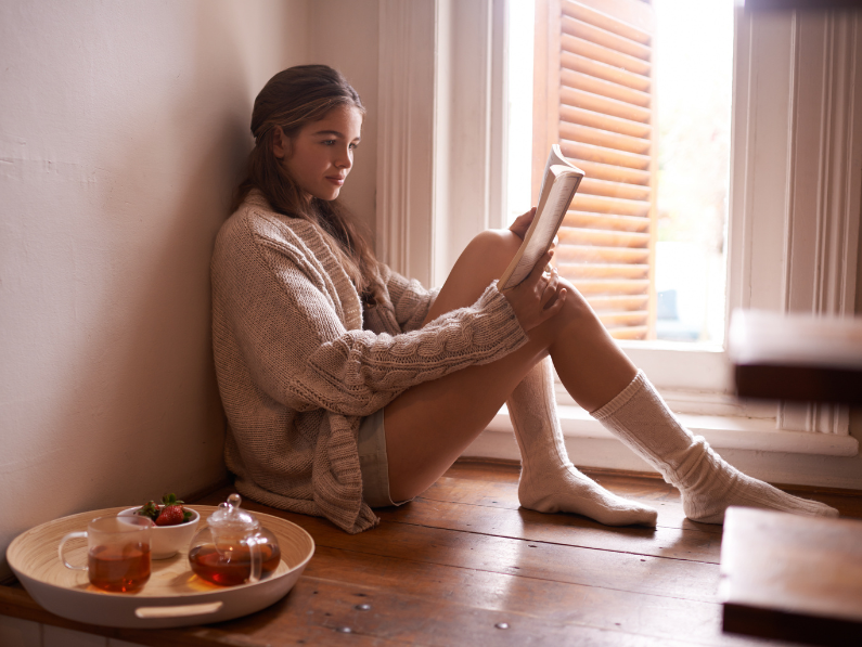 photo of woman sitting on the floor with a tray of tea beside her enjoying a spooky reading session