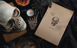 photo of spooky detritus with skeleton, pomegranate and aged paper that says halloween