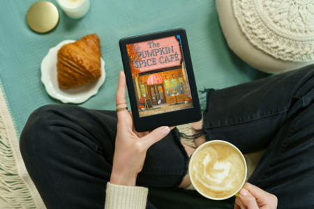 photo of woman reading the book the pumpkin spice cafe by laurie gilmore on an e-reader with a croissant and latte