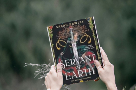 photo of woman holding book servant of earth by Sarah Hawley above trees outside