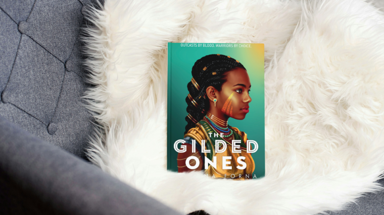 photo of book the gilded ones by namina forna sitting on a white throw blanket in a grey chair