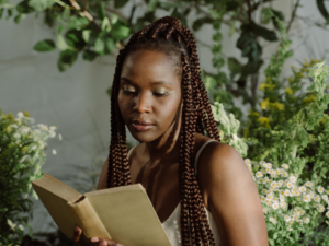 photo of black woman with braids reading a book in a room with flowers